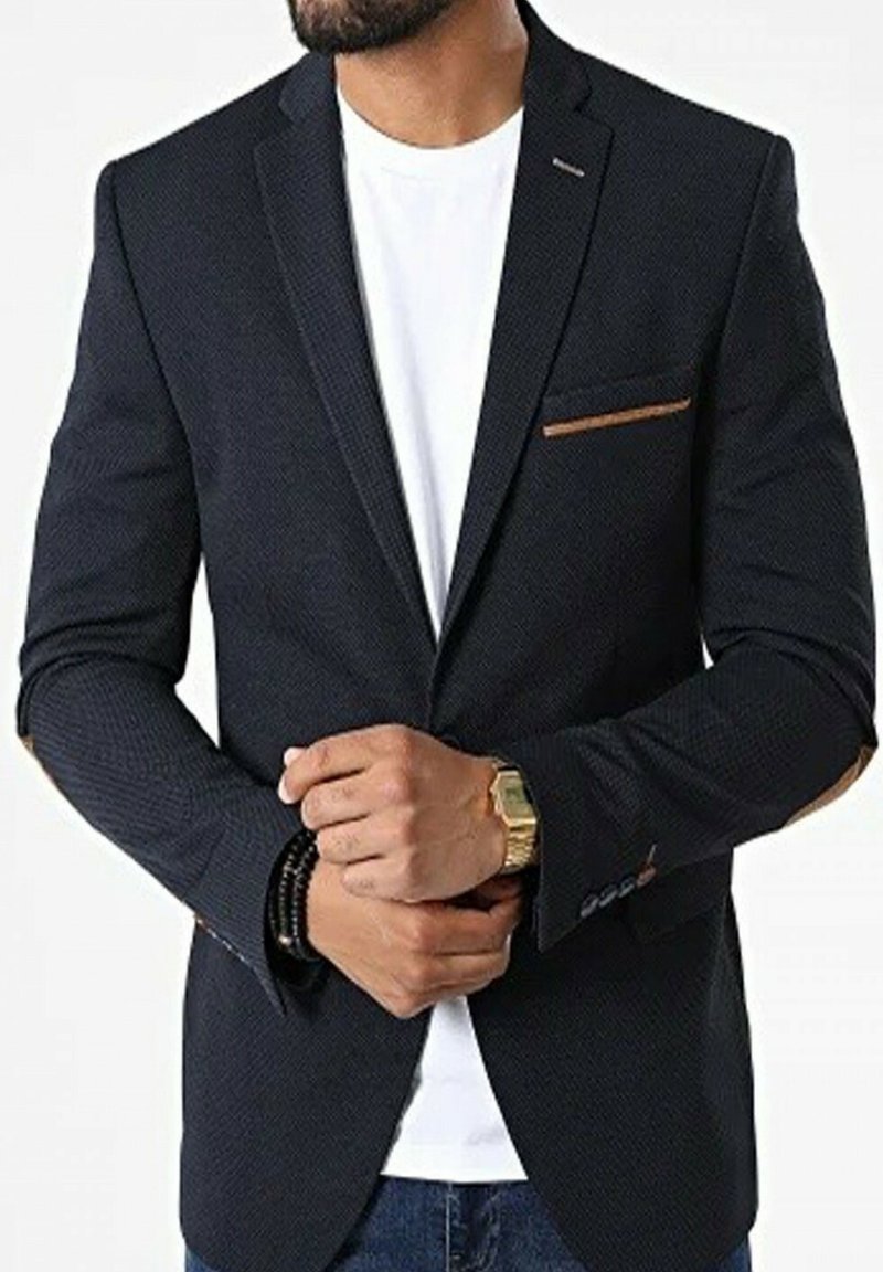Blazer bleu marine foncé en tissu texturé, avec un détail de poche en brun contrasté, coupe ajustée et revers en notches, porté sur une chemise blanche.