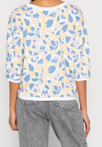 Top in cotone leggero con maniche a tre quarti, caratterizzato da un motivo floreale pastello nei toni di blu, giallo e rosa, con colletto e polsini bianchi.