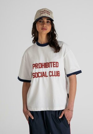 Biała bawełniana koszulka z granatowymi akcentami i wyraźnym czerwonym napisem "PROHIBITED SOCIAL CLUB", zestawiona z beżową czapką w paski.