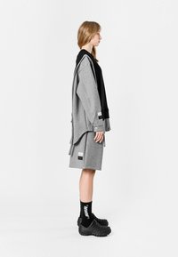 Sudadera gris de gran tamaño superpuesta sobre una base negra, combinada con una falda gris a juego. Zapatos negros texturizados y calcetines negros con letras blancas.