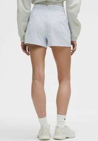Bermudas de color azul claro con cinturilla elástica, que presentan una textura suave y un corte casual, combinadas con zapatillas blancas y calcetines.
