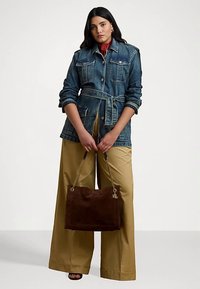 Denim jacket with a belted waist, two chest pockets, and rolled sleeves. Wide beige pants and a brown suede handbag with gold hardware.