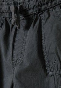 Svarta shorts med elastisk midja och dragsko, med sidofickor och en mjuk, lätt tygtextur. Synliga sömmar.
