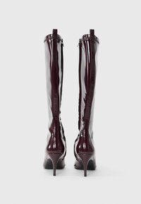 Bordeaux gepatineerde leren kniehoge laarzen met spitse neuzen en een stilettopunt. Bevat een ritssluiting aan de achterkant. Glad, glanzend textuur.