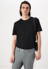 Black short-sleeve t-shirt paired with gray checkered trousers. Trousers feature a front button closure and a side strap bag.