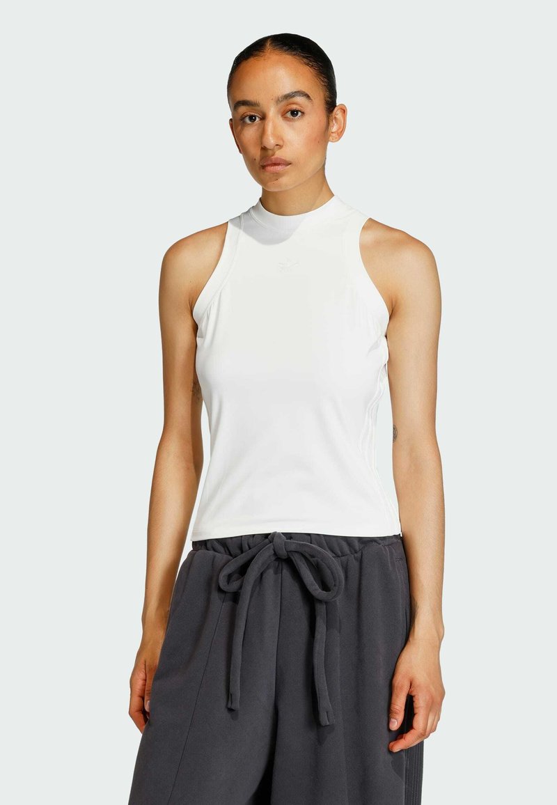 Biela bezrukávová blúzka s vysokým výstrihom, hladkou textúrou a minimalistickým dizajnom. Skombinovaná s tmavými, voľnými nohavicami s viazaním.