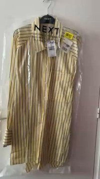 Camicia a maniche lunghe a righe gialle con tasca, realizzata in tessuto leggero. Etichette attaccate, appesa in una confezione di plastica trasparente.
