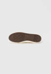 Rubberen sneakerzool met een gestructureerde bruine basis, crème-kleurige randen en een patroon voor grip. Vlak en licht afgeronde vorm.