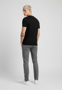 Czarny krótki rękaw t-shirt o dopasowanym kroju, zestawiony z jasnoszarymi spodniami i białymi trampkami, widziany od tyłu.