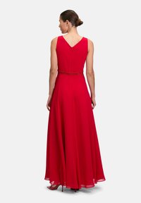 Rotes ärmelloses Kleid mit V-Ausschnitt, fließendem Rock und verziertem Bund. Hergestellt aus leichtem Stoff, mit einem Reißverschluss auf der Rückseite.