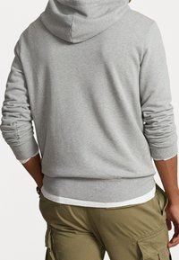 Felpa grigia con cappuccio, dal taglio morbido, con polsini e orlo a costine. Il materiale ha una texture liscia. Indossata con pantaloni cargo color khaki.