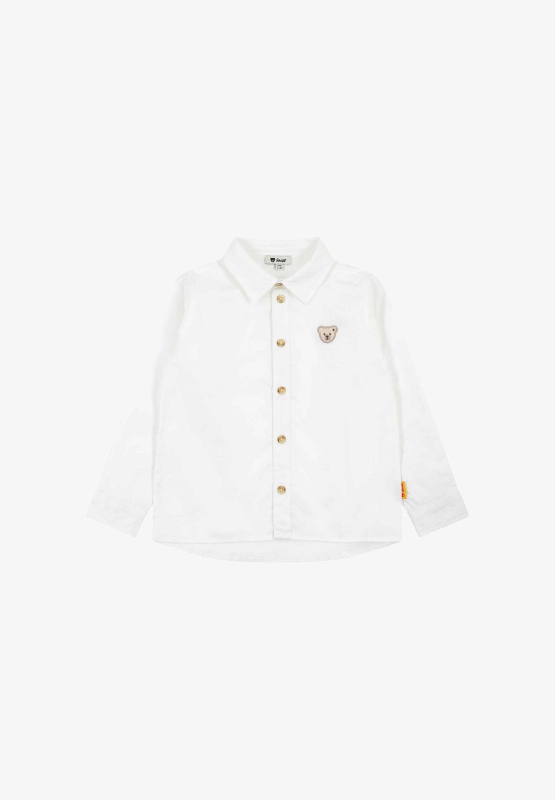 Chemise blanche à manches longues pour tout-petit, avec col et petite écusson ourson sur la poitrine, équipée de boutons marron.