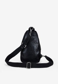 Bolso de cuero negro con una superficie texturada, que cuenta con una amplia correa de tela ajustable y acentos en metal plateado. Forma compacta y triangular.