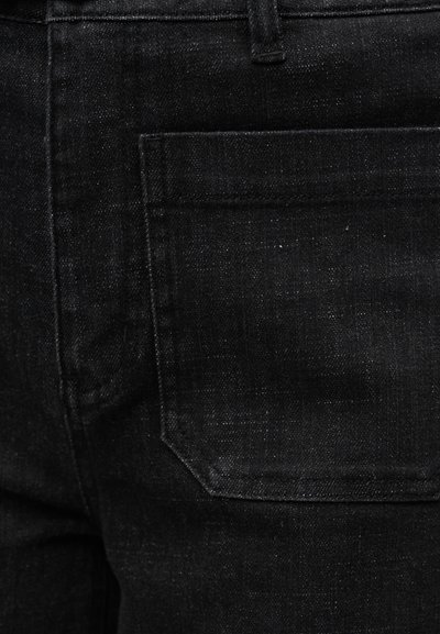 Μαύρο τζιν denim κοντινή λήψη που δείχνει λεπτομέρειες της πίσω τσέπης και της θηλιάς της ζώνης με ορατή υφή ραφής.