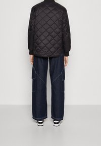 Schwarze gesteppte Jacke mit Rautenmuster und gerippten Bündchen, kombiniert mit weit geschnittenen Denim-Cargo-Hosen mit Seitentaschen und kontrastierenden Nähten.