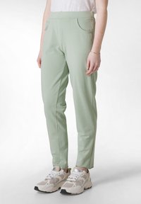 Lichtgroene stretchy broek met twee voorkeurszakken, taps toelopend ontwerp en een gladde textuur, gecombineerd met witte en beige sneakers.