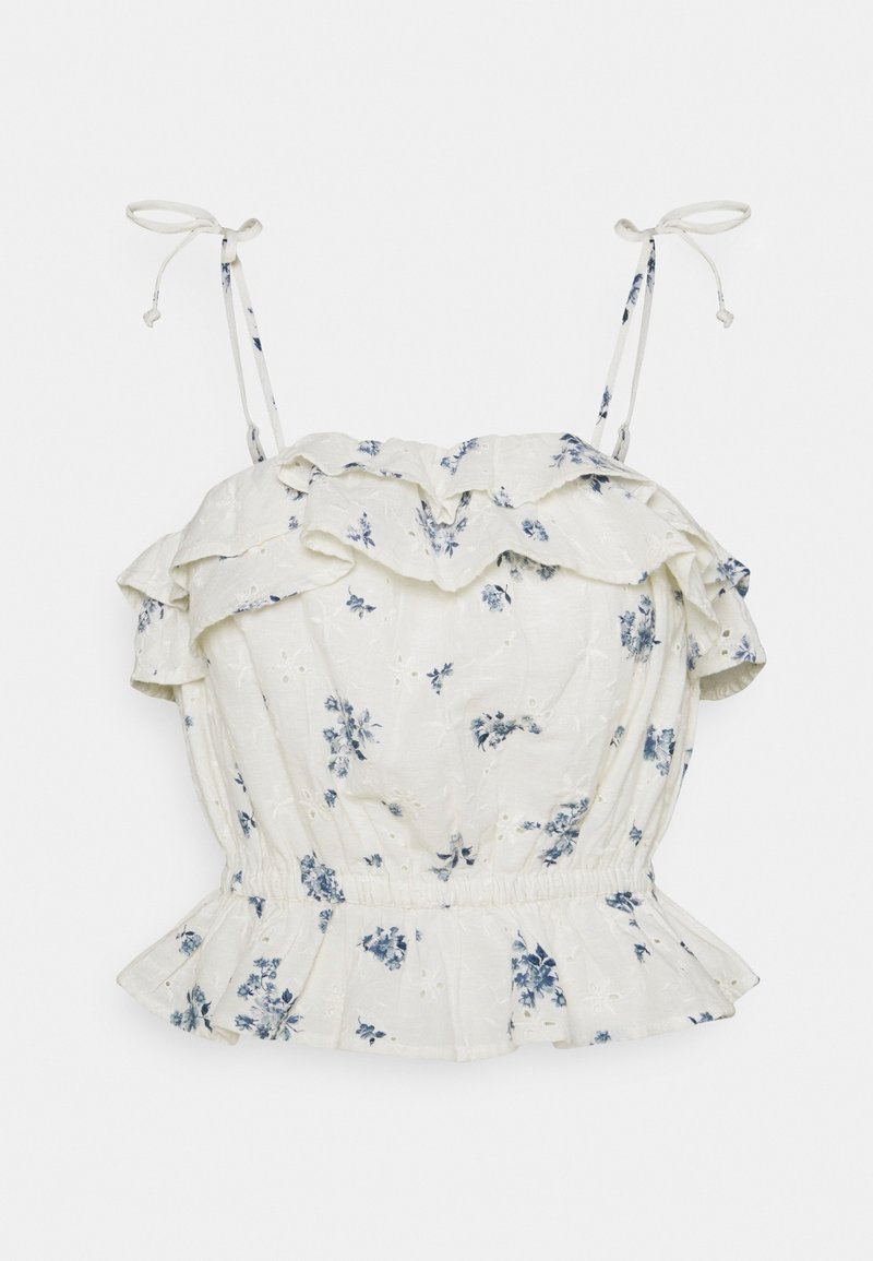 Blouse blanche sans manches avec imprimé floral bleu, col froncé et ourlet volanté, et bretelles réglables à nouer.