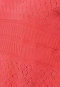 Υφασμα κοραλλί με υφή που παρουσιάζει διαμάντι και ραβδώσεις, συνδυάζοντας ομαλές και ανάγλυφες υφές με ομοιόμορφο χρώμα.