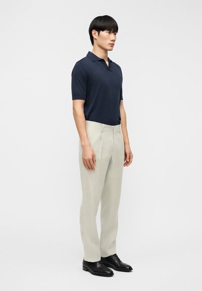 Polo de manga corta azul marino combinado con pantalones gris claro, con un corte entallado y zapatos de cuero negro. Diseño sencillo y limpio.