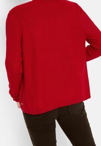 Cardigan rosso lavorato a maglia con superficie testurizzata, maniche lunghe e scollatura rotonda. Presenta lati leggermente svasati e orlo a costine.