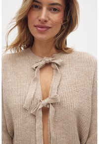 Cardigan a maglia beige con scollatura a V e lacci al centro davanti. Presenta un motivo testurizzato e un aspetto morbido e leggero.