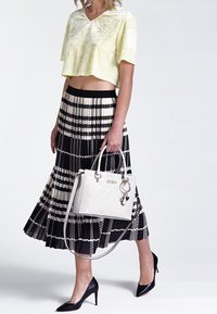 Lys gul cropped top, sort plisseret nederdel med hvide geometriske mønstre, sorte højhælede sko og en hvid kviltet taske.