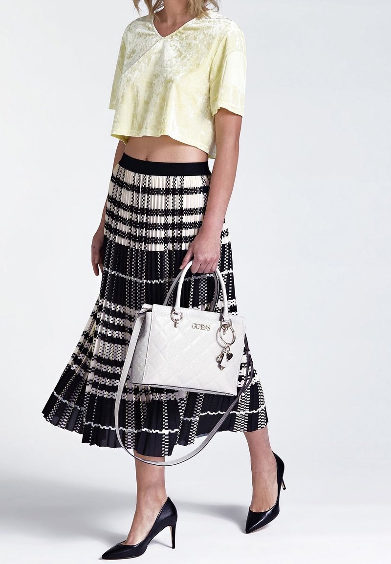 Lys gul cropped top, sort plisseret nederdel med hvide geometriske mønstre, sorte højhælede sko og en hvid kviltet taske.