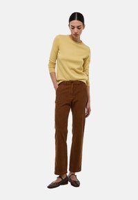 Pull jaune ajusté, pantalon en velours côtelé marron avec une finition texturée, et chaussures en cuir tressé marron foncé. Tenue décontractée avec une coupe confortable.