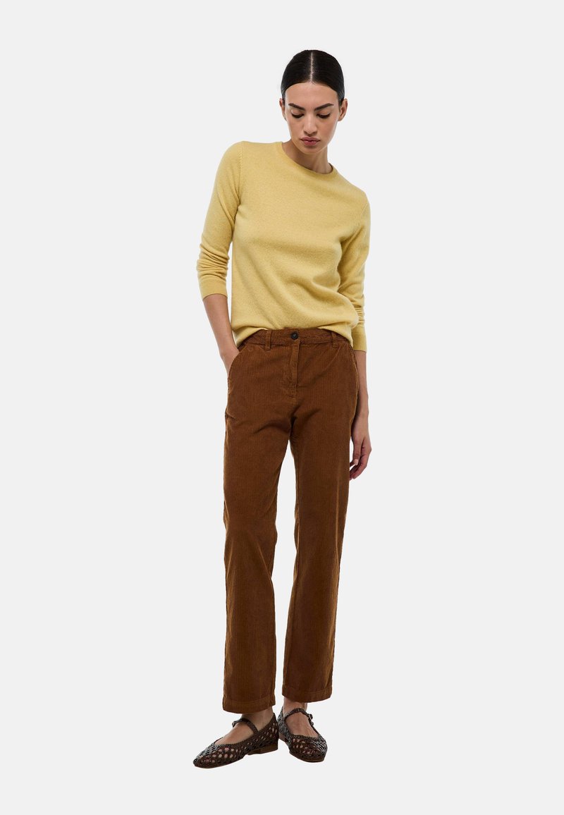 Pull jaune ajusté, pantalon en velours côtelé marron avec une finition texturée, et chaussures en cuir tressé marron foncé. Tenue décontractée avec une coupe confortable.