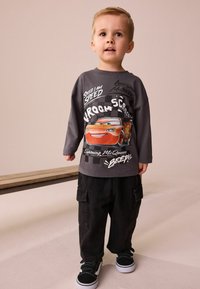 Šedá dlouhá tričko s barevným grafickým motivem Bleska McQueena a textem. V kombinaci s volnými černými cargo kalhotami a černými teniskami.