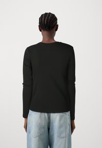 Schwarzes Langarmshirt mit Rundhalsausschnitt, aus glattem Stoff. Getragen mit hellblauen weiter geschnittenen Jeans. Schlichtes und körperbetontes Design.