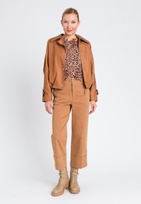 Giacca cropped marrone, top con stampa animale, pantaloni beige a vita alta e stivali militari color sabbia. Tessuto liscio con vestibilità rilassata e dettagli con bottoni.