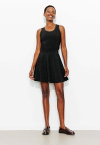 Haut noir sans manches avec une taille cintrée, associé à une jupe noire évasée. Le mannequin porte des mocassins marron. Texture lisse, sans motifs.