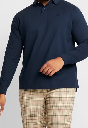 Polo de manga larga de color azul marino con cuello, que presenta un detalle de logo. Se lleva con pantalones de patrón a cuadros claro. Material de algodón.