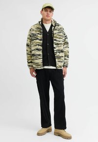 Fleece jakas ar viļņainu melnu un beigu rakstu, apvienota ar melnu džemperi, melniem korduroja biksēm un beigu kurpēm. Viegls cepure uz galvas.
