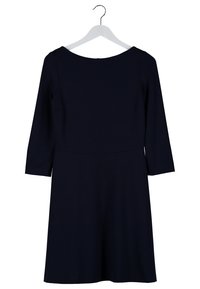 Robe noire longueur genou avec manches trois-quarts accrochée à un cintre blanc sur fond blanc.