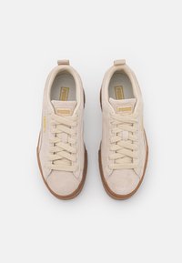 Baskets en suède beige avec bout rond, semelle en caoutchouc texturée, lacets crème et accents en or sur la languette et sur le côté.