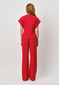Rood twee-delig outfit met een gestructureerde top met korte mouwen en wijde broekspijpen. Gladde stof met een effen kleur, geen zichtbare patronen.