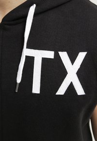 Hoodie nero con stampa bianca "TX", con cordini bianchi a contrasto e finitura testurizzata.