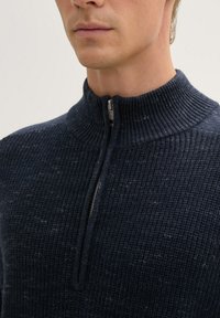 Pulover tricotat bleumarin cu guler înalt și fermoar pe jumătate, având un model texturat și străluciri vizibile în întreaga țesătură.