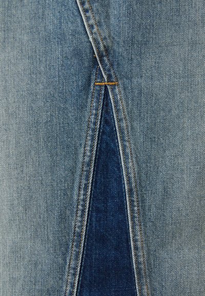 Gai zils denims ar neapstrādātu griezumu, kas atklāj tumšāku denim audumu zem tā. Iezīmējas ar kontrastējošu oranžu diegu gar šuvēm.