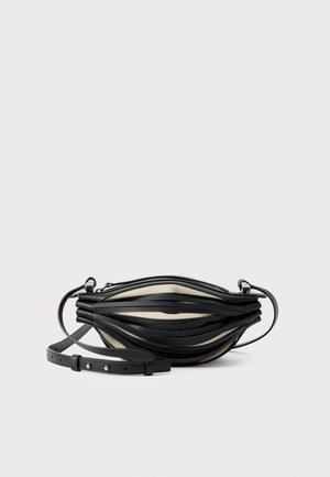 Pequeño bolso cruzado negro y beige con correas de cuero en capas y correa ajustable con hebilla sobre fondo blanco.