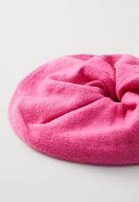 Roze gebreide scrunchie met een zachte, gestructureerde oppervlakte, ronde vorm en een licht geplooid ontwerp, rustend op een lichte achtergrond.