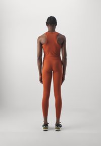 Orangefarbener, sportlicher Tanktop und Leggings mit figurbetontem Design. Glatte Textur, minimales Branding, getragen mit schwarzen Laufschuhen.