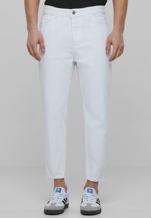 Jeans in denim bianco con taglio dritto, cinque tasche e chiusura con bottone. Indossati con sneakers grigie e nere con accenti blu.
