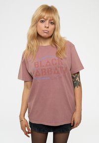 Pink oversized t-shirt made of cotton, featuring the words "BLACK SABBATH" in a distressed red font with blue accents, short sleeves, and a round neckline.