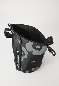 Black bucket bag with floral pattern in gray tones, made of fabric, featuring a zip closure and a detachable strap with logo.