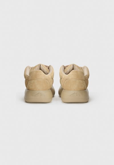 Beige suede low-top shoes with a padded collar, soft leather lining, and rubber outsole, featuring a subtle logo on the heel.