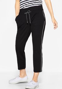 Czarne spodnie dresowe z elastycznym paskiem, z bocznymi kieszeniami i kontrastującymi białymi paskami wzdłuż nogawek. Gładka tekstura materiału.
