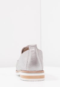 Chaussure en cuir argenté perforé avec un bout arrondi et une semelle en caoutchouc, présentant un accent en bois naturel contrastant à la base.